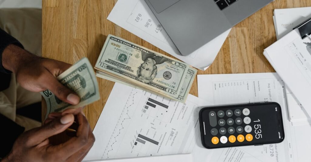 Close-up of hands counting cash on desk with calculator, charts, and laptop, illustrating financial management.