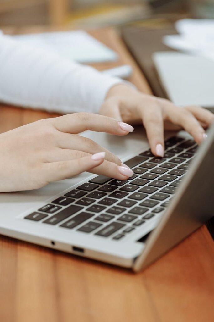 Close-up of a woman's hands typing on a laptop next to a coffee cup in a casual setting.