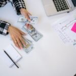 Businesswoman counting dollar bills with financial charts and laptop on table. Investment and finance concept.